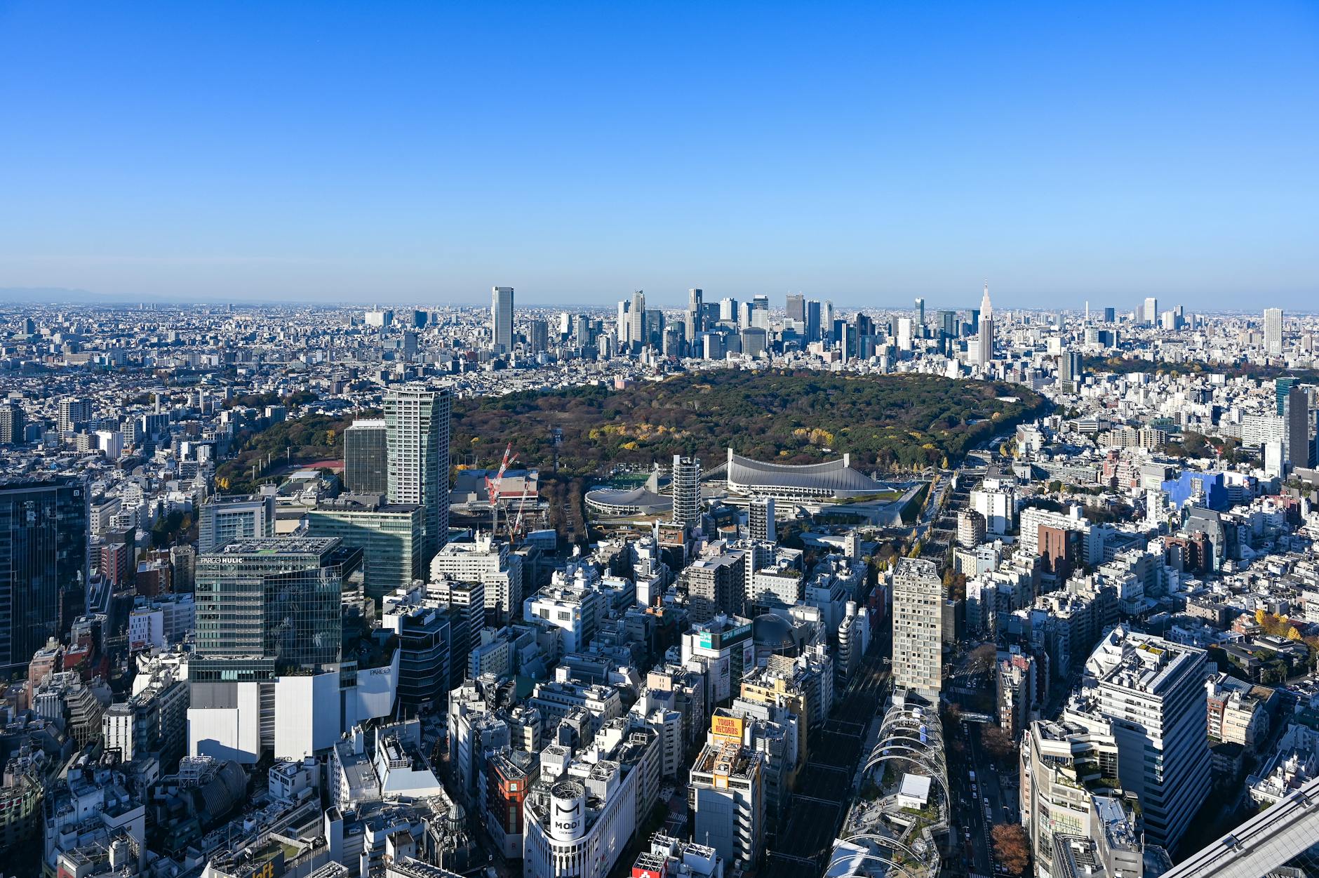 Aerial view of Tokyo cityscape featuring Shinjuku Park surrounded by skyscrapers under a clear blue sky. – foto door Laser Cheung via Pexels